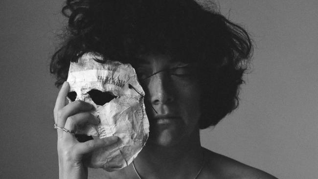 A person holds a papier mache facemask alongside their face