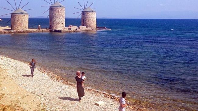 Four refugees, including a mother holding a child, by the shore in Chios, Greece